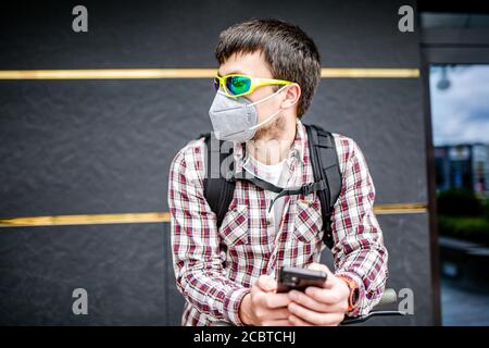 Männlicher Kurier trägt Schutzmaske Gesicht angekommen Lieferadresse auf Elektroroller. Subject Lieferung während covid 19 auf Umwelt Stockfoto