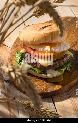 Street Food, Fast-Pub-Essen. Hausgemachte saftige Burger mit Rind, Käsestomate, Salat und Eierzwiebeln auf Holztisch. Scharfes Licht für die Sommerernte moo Stockfoto