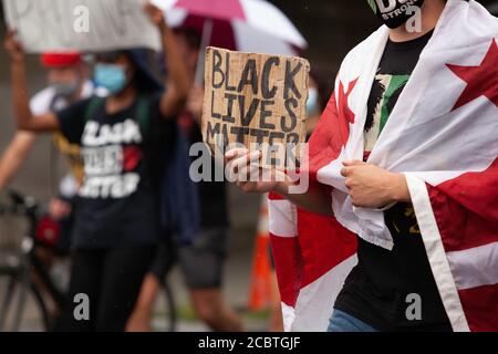 Washington, DC, USA. 15. August 2020. Im Bild: Ein Protestler bei der Entfinanzierung des Polizeimarsches trägt ein Schild, das sagt, "Black Lives Matter", während in der Flagge des Distrikts von Columbia drapiert. Kredit: Allison C Bailey/Alamy Gutschrift: Allison Bailey/Alamy Live Nachrichten Stockfoto