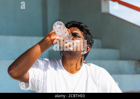 Nahaufnahme asiatische junge Sportläufer schwarz Mann tragen Athlet Kopfhörer er Trinkwasser aus einer Flasche nach dem Laufen an Der Outdoor Street Health Park Stockfoto