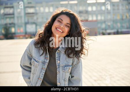 Happy African Mädchen tragen Denim Jacke Blick auf Kamera auf der Straße stehen. Stockfoto