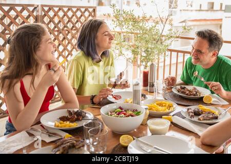 Zwei Mädchen im Teenageralter und ein Mann mittleren Alters essen und lachen am Esstisch. Familienkonzept von Familie Essen und Spaß zusammen haben Stockfoto