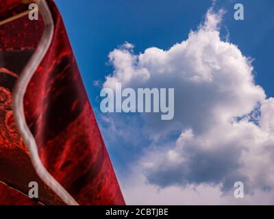 Ein roter Sonnenschirm gegen einen blauen Himmel mit einem großen Weiße, flauschige Wolke Stockfoto