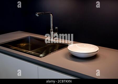 Schwarze Spülbecken und Leitungswasser in der Küche. Das Innere des Küchenraums der Wohnung. Haushaltsgeräte. Weiße Teller Stockfoto
