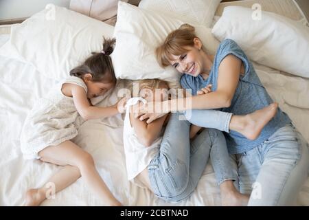 Freundlich lachende Mutter und Töchter kitzeln und spielen auf dem Bett Stockfoto
