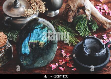 Labradorit Kristall auf dunklem Holztisch mit verschiedenen Naturobjekten wie getrockneten immergrünen, Pflanzen, Blumen, Kräutern im Hintergrund Stockfoto