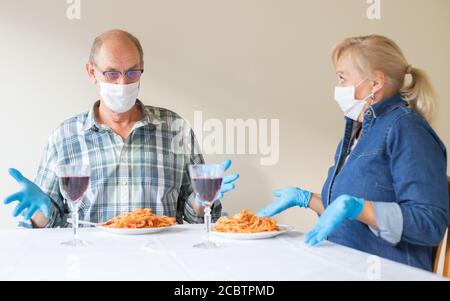 Ältere Paare schauen überrascht zu ihrem Abendessen, sie tragen weiße medizinische Schutzmasken - Coronavirus Schutz Maßnahmen Konzept (AT-Restaurant Stockfoto