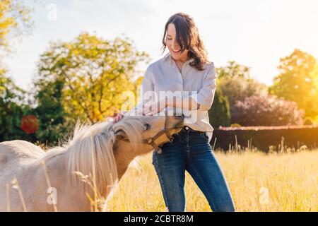 Porträt von jungen lächelnden Frau streicheln weißen Pony im Freien Stockfoto