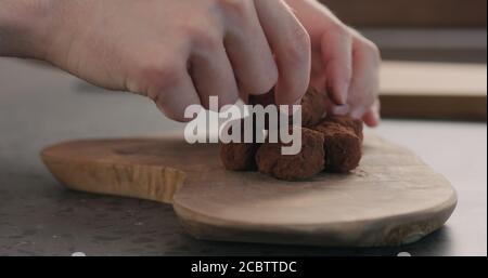 Man Hand legte handgemachte Schokolade Trüffel auf einem Holzbrett, breites Foto Stockfoto