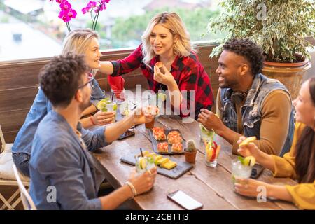 Multirassische Gruppe junger Millennials Freunde, die miteinander reden und essen - Studenten Party auf dem Dach Café Stockfoto