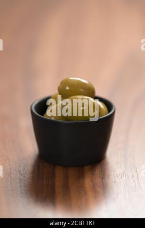 Riesige grüne Oliven in schwarzer Schüssel auf Walnusstisch, flacher Fokus Stockfoto