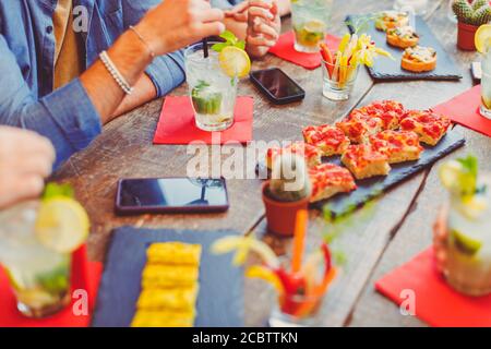 Beschnittenes Bild von Leuten, die am Tisch sitzen und Cocktails trinken Abendessen mit Pizza und Vorspeisen Stockfoto