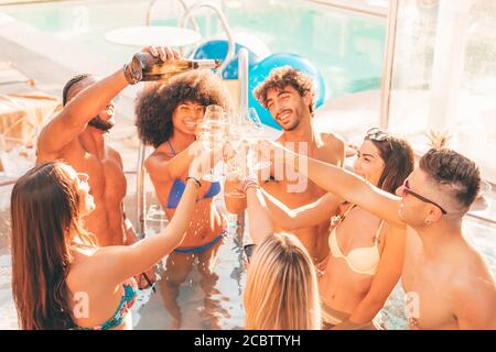 Multirassische Gruppe von jungen Freunden toasting auf Sommer Pool Party, trinken Champagner oder Wein und Spaß zusammen Stockfoto