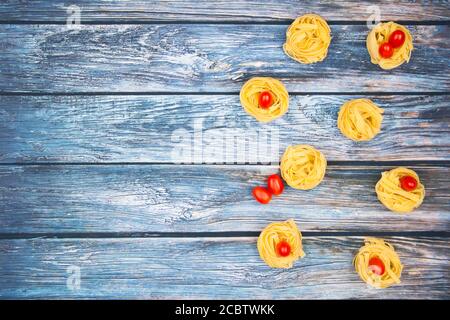 Nahaufnahme von Nestern von Tagliatelle Nudeln mit Ei-förmigen Mini roma Tomaten auf einem rustikalen Holztisch mit Sackleinen, Stockfoto