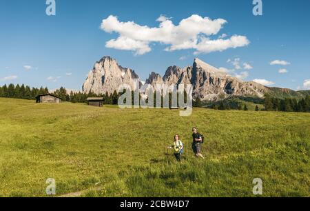 Zwei Wanderer wandern auf den grünen Wiesen der Seiser Alm Im Sommer mit schroffem Langkofel im Hintergrund Stockfoto