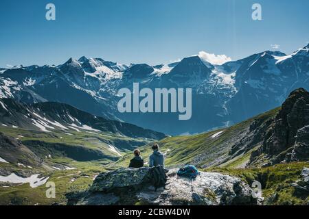 Zwei Wanderer sitzen auf der Spitze eines Berges, entspannen und genießen Sie eine malerische Aussicht Stockfoto