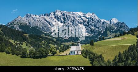 Panorama von grünen Wiesen und Pfarrkirche Dienten mit Hochkönig im Hintergrund. Pinzgau, Salzburg, Österreich. Stockfoto