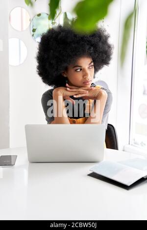 Nachdenklich afrikanisches Mädchen, das durch das Fenster schaut, das am Kaffeetisch sitzt, benutzen Laptop. Stockfoto