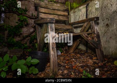 Verfallende hölzerne Gartenstuhl in der vergessenen Ecke verlassen Der Garten Stockfoto