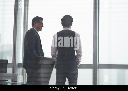 Rückansicht von zwei asiatischen Geschäftsleuten, die davor standen Des Bürofensters mit einer Diskussion Stockfoto