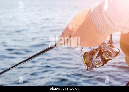 Angeln auf dem See. Hände des Fischers mit Angelrute und Haspel. Makroaufnahme. Angelrute und Hände des Fischers über dem Seewasser. Spinnrute. Fishi Stockfoto