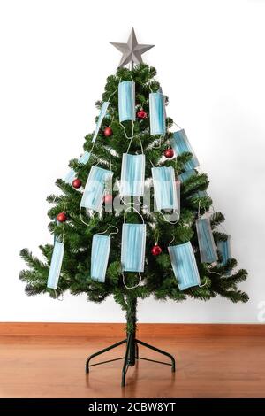 Vertikales Farbbild mit einer Vorderansicht eines Weihnachtsbaums, geschmückt mit roten Kugeln, blauen Coronavirus-Masken und einem großen Stern. Covid und glückliches neues Jahr c Stockfoto