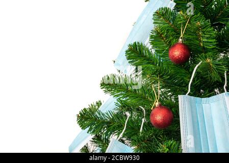 Horizontales Farbbild mit einer Vorderansicht eines Weihnachtsbaums, der mit roten Kugeln und blauen Coronavirus-Masken geschmückt ist. Covid und glückliches neues Jahr Konzept. Stockfoto