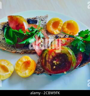 Sehr gesundes vegetarisches Frühstück oder Brunch, Lieblingsgericht. Selbstgebackenes Brot mit Olivencreme, eigene schwarze Zebratomaten und frische Aprikosen mit Petersilie Stockfoto