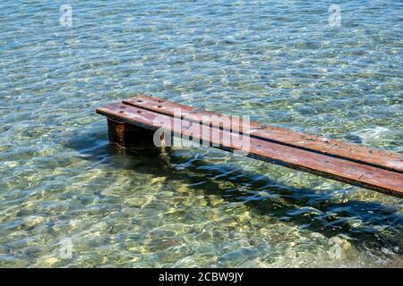 Verwitterter Holzsteg in Kea, Insel Tzia, Griechenland. Holzplanken richtig auf rostigen Lauf gesetzt, um eine Mini-Plattform über einem transparenten ruhigen Blau zu machen Stockfoto