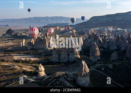 Heißluftballons schweben durch die Landschaft der Feenkamine, wenn die Sonne in der Nähe von Goreme in der Region Kappadokien in der Türkei aufgeht. Stockfoto