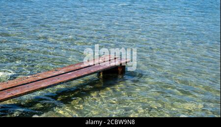 Verwitterter Holzsteg in Kea, Insel Tzia, Griechenland. Holzplanken richtig auf rostigen Lauf gesetzt, um eine Mini-Plattform über einem transparenten ruhigen Blau zu machen Stockfoto