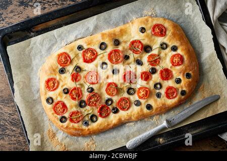 Focaccia, Pizza, italienisches Fladenbrot mit Tomaten, Oliven und Rosmarin auf Tablett Stockfoto