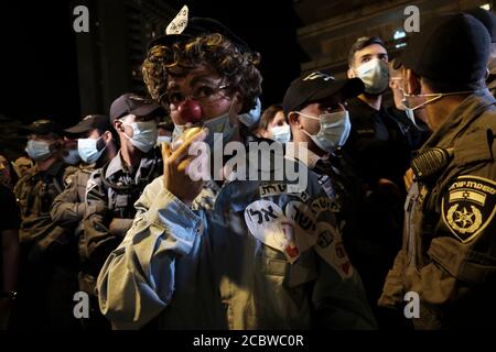 JERUSALEM, ISRAEL - AUGUST 15: Ein Protestler mit Polizeikostüm und einer roten Nase eines Clowns steht inmitten von Polizisten, während sie während einer Massendemonstration, an der über 15000 Personen im Rahmen der laufenden Demonstrationen gegen Premierminister Benjamin Netanjahu wegen seiner Anklage wegen Korruptionsvorwürfen und des Umgangs mit der Coronavirus-Pandemie im Freien teilnahmen, wachen Offizielle Residenz des Premierministers am 15. August 2020 in Jerusalem, Israel. Stockfoto