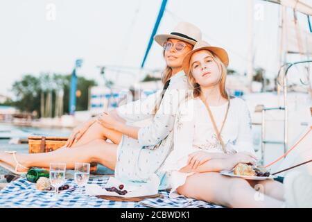Zwei schöne blonde Mädchen Freunde Mutter und Tochter in weiß Und Strohhüte mit Picknick auf der Yacht am Pier Stockfoto