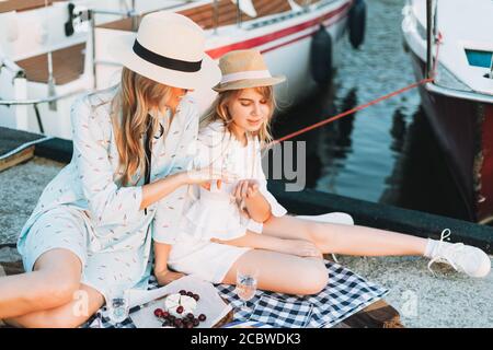 Zwei schöne blonde Mädchen Freunde Mutter und Tochter im Stroh Hüte beim Picknick auf dem Jachtpier Stockfoto