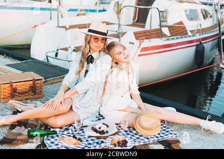 Zwei schöne blonde Mädchen Freunde Mutter und Tochter im Stroh Hüte beim Picknick auf dem Jachtpier Stockfoto