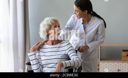 Lächelnde junge Krankenschwester kümmert sich um glückliche behinderte ältere Patienten. Stockfoto