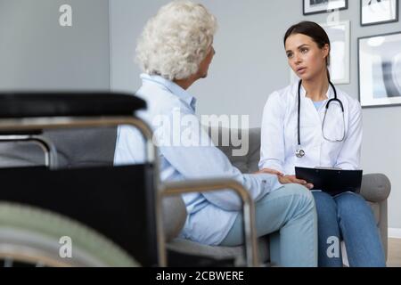 Junge fokussierte Krankenschwester besucht behinderte Patienten zu Hause. Stockfoto