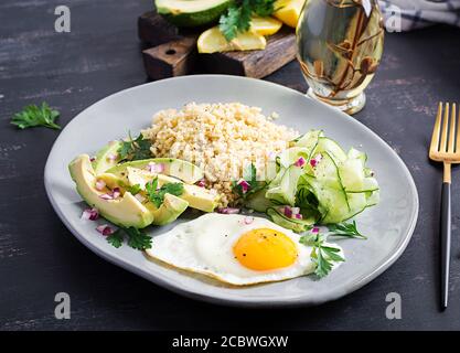 Diät-Menü. Gesunder Lebensstil. Bulgur-Brei, Spiegelei und frisches Gemüse - Gurke und Avocado auf dem Teller. Stockfoto