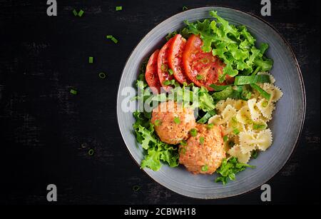 Italienische Pasta. Farfalle mit Fleischbällchen und Salat auf dunklem Hintergrund. Abendessen. Draufsicht, Overhead. Slow Food Konzept Stockfoto