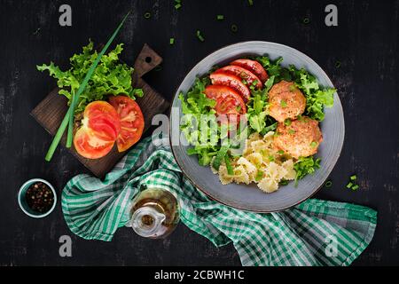 Italienische Pasta. Farfalle mit Fleischbällchen und Salat auf dunklem Hintergrund. Abendessen. Draufsicht, Overhead. Slow Food Konzept Stockfoto