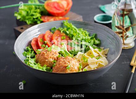 Italienische Pasta. Farfalle mit Fleischbällchen und Salat auf dunklem Hintergrund. Abendessen. Slow Food Konzept Stockfoto