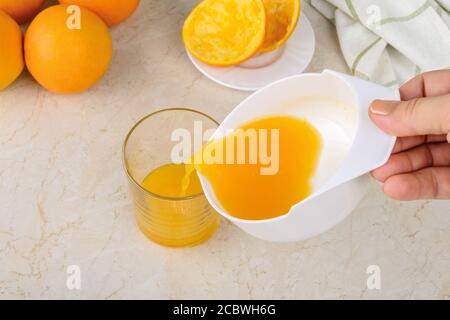 Kaukasische Frau Hände Gießen frisch gepressten Orangensaft aus manuellen Zitruspresse in ein Glas auf einem Küchentisch. Vegetarische, Rohkost Ernährung Stockfoto