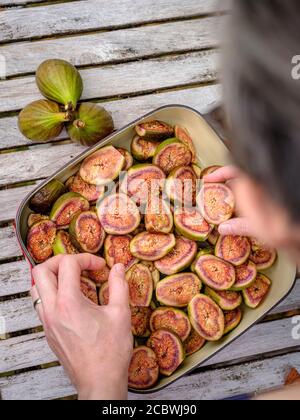 Eine Frau, die in einem Landgarten im Südosten Großbritanniens eine Rösterschale mit halbierten, selbst angebauten Feigen anstellt, August. Stockfoto