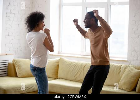 Aktives junges afrikanisches Paar, das im Wohnzimmer zu Hause tanzt Stockfoto