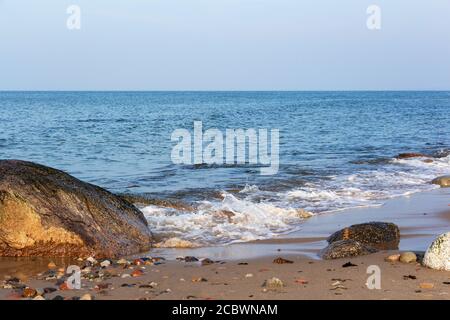 An einem sonnigen Tag trifft eine schöne Welle auf die Felsen an einem Sandstrand. Stockfoto