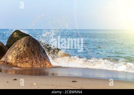 An einem sonnigen Tag trifft eine schöne Welle auf die Felsen an einem Sandstrand. Stockfoto