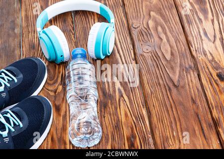 Sportausrüstung. Sneaker, Wasser und Kopfhörer auf Holzhintergrund Stockfoto