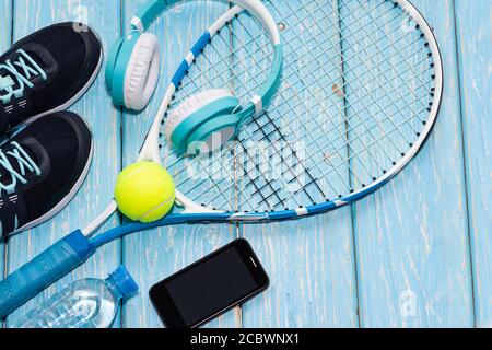 Tennisschläger. Hellblauer Hintergrund. Turnschuhe, Rakete, Ball, Wasserflasche, Musik-Kopfhörer. Stockfoto