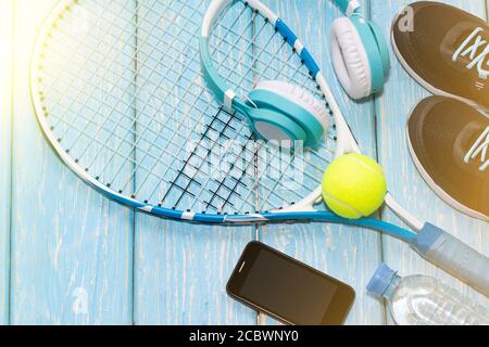 Tennisschläger. Hellblauer Hintergrund. Turnschuhe, Rakete, Ball, Wasserflasche, Musik-Kopfhörer. Stockfoto